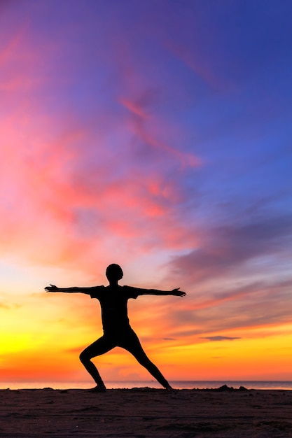 Silhouette jeune femme pratiquant le yoga sur la plage au coucher du soleil.