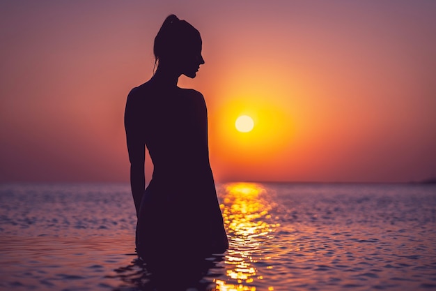 silhouette de jeune femme pratiquant le yoga sur la plage au lever du soleil