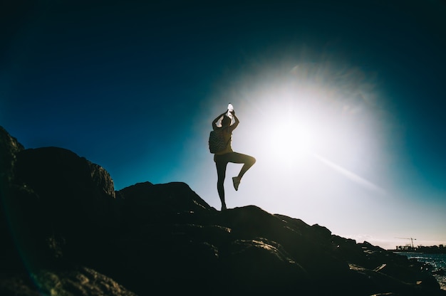 Silhouette d&#39;une jeune femme pratiquant le yoga sur une rive rocheuse