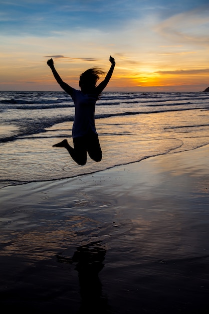 Silhouette d&#39;une jeune femme volant dans le ciel au coucher du soleil sur la mer