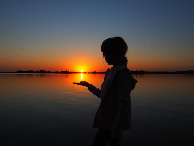 Silhouette d'une jeune fille sur fond de coucher de soleil L'enfant tient le soleil couchant sur sa main