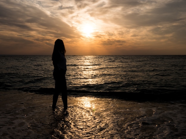 Silhouette d'une jeune fille sur la plage. jeune fille marche au coucher du soleil au bord de la mer. Fille de touristes sur la plage pendant les vacances