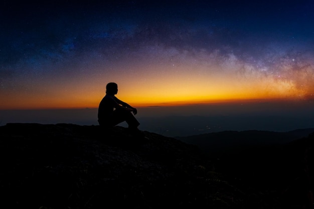 Silhouette de jeune homme assis sur le dessus de la montagne seul au lever du soleil Regardez le ciel