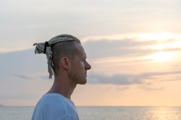 Silhouette d'un jeune homme avec des dreadlocks sur la tête près de la mer pendant le coucher du soleil. Portrait en gros plan. Heureux bel homme avec des dreadlocks sur la plage tropicale