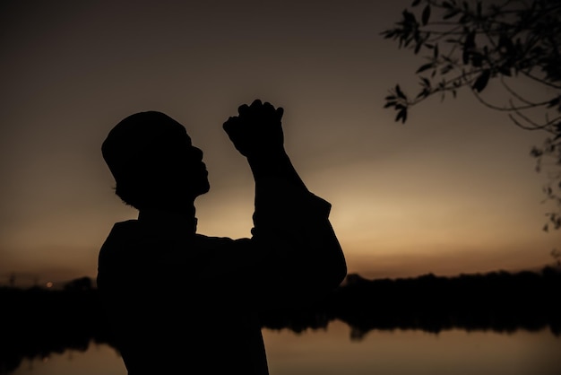 Silhouette Jeune homme musulman asiatique priant au coucher du soleil Concept du festival Ramadan