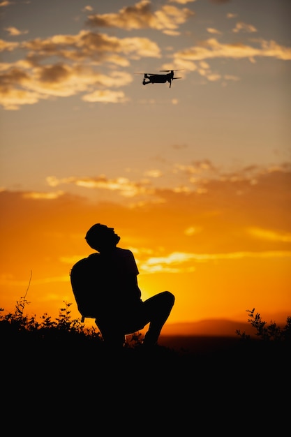 Silhouette d'un jeune homme avec un sac à dos d'exploitation d'un drone dans un cadre rural au coucher du soleil