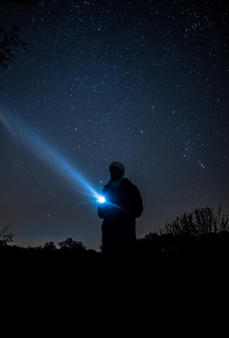 Photo silhouette d'un jeune homme tenant une lampe de poche alors qu'il se tient sur un champ contre un champ d'étoiles la nuit