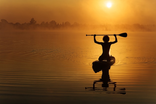 Silhouette de jeune sportif actif nageant sur paddle board sur le lac local.