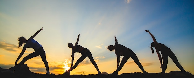 Silhouette de jeunes femmes pratiquant le yoga ou le pilates au coucher ou au lever du soleil dans un bel endroit de montagne.