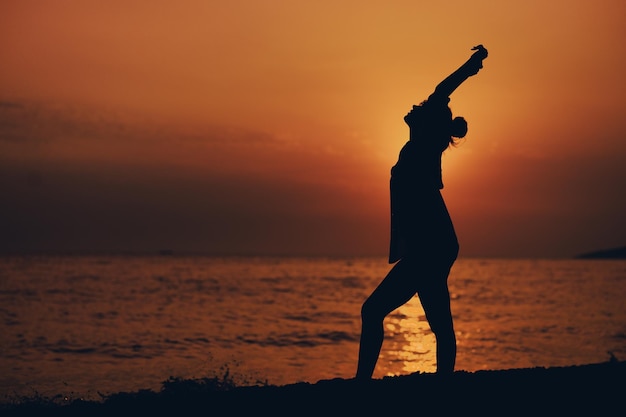 Silhouette d'une jolie jeune femme posant sur la plage pendant le coucher du soleil