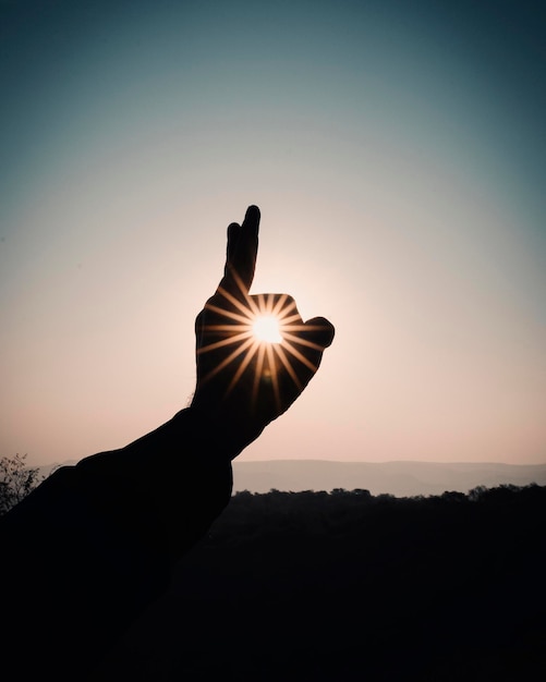 Photo silhouette de la main faisant un geste contre le soleil au coucher du soleil