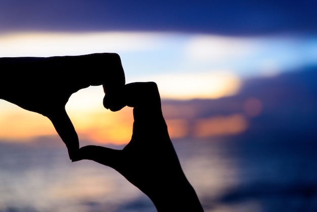 Silhouette les mains de femme pour être en forme de cœur sur fond de coucher de soleil.