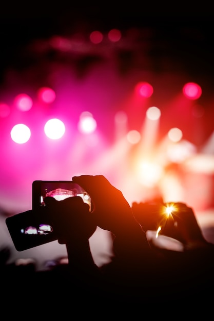 Silhouette de mains utilisant des smartphones pour prendre des photos et des vidéos lors d'un spectacle de musique en direct.