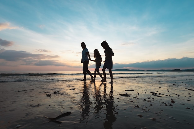 Silhouette de mère asiatique et de deux filles tenant la main et marchant sur la plage ensemble au moment du coucher du soleil avec une belle mer et ciel. Profitez de la famille avec le concept de la nature.