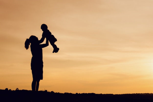 Silhouette de mère et fille, soulever des enfants dans l&#39;air au ciel coucher de soleil pittoresque à riverside.