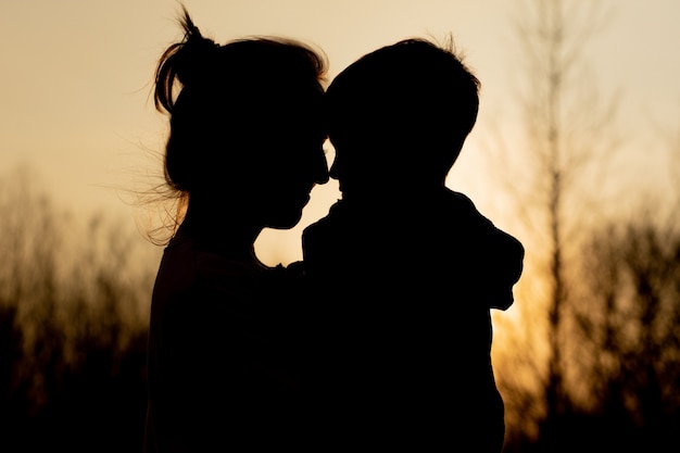Silhouette d'une mère et son fils jouant à l'extérieur au coucher du soleil. Concept de fête des mères