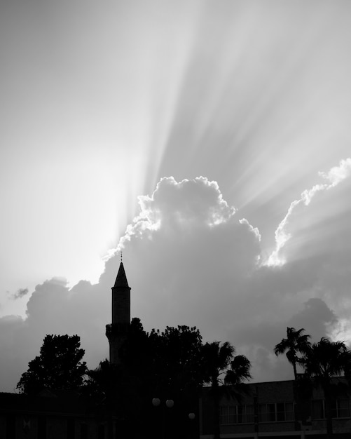 Photo silhouette de mosquée avec minaret et ciel avec des rayons de lumière au-dessus, photographie en noir et blanc