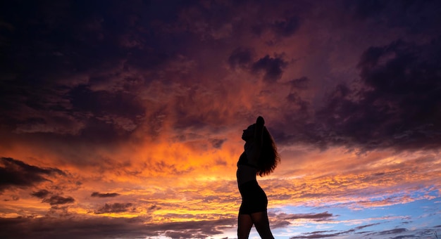Silhouette noire de jolie fille ou belle femme modèle mince sexy avec de longs cheveux pose sur la plage de la mer au coucher du soleil à l'extérieur sur fond de ciel violet