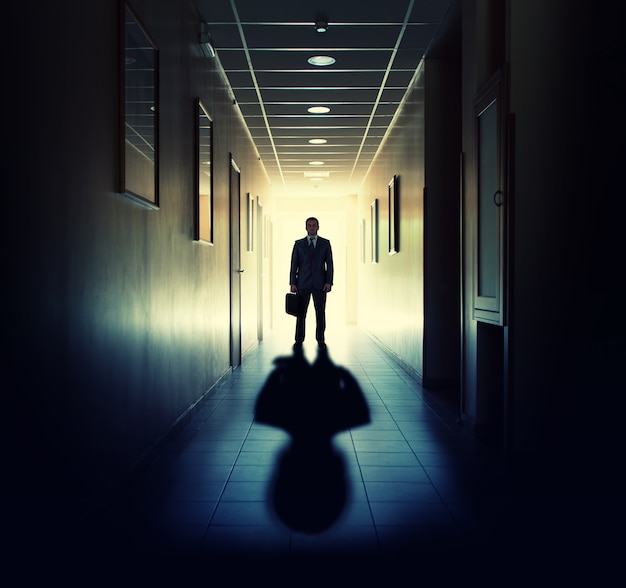 Silhouette of businessman standing in office building corridor contre la lumière