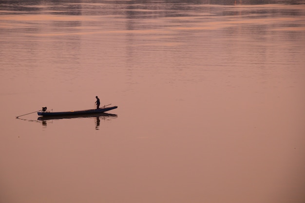 Silhouette de pêcheur en bateau sur la rivière. Concept de tons chauds.