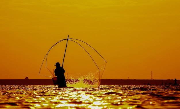Silhouette de pêcheurs à l'aide d'outils de pêche et pendant le soleil d'or brille