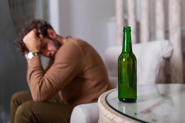 Silhouette de personne alcoolique anonyme buvant derrière une bouteille d'alcool. Homme combattant avec des habitudes alcooliques, buvant assis sur un canapé à la maison