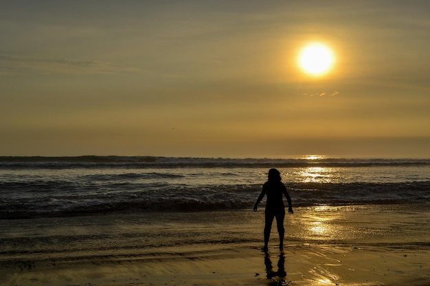 silhouette d'une personne au bord de la mer à l'heure d'or du coucher du soleil