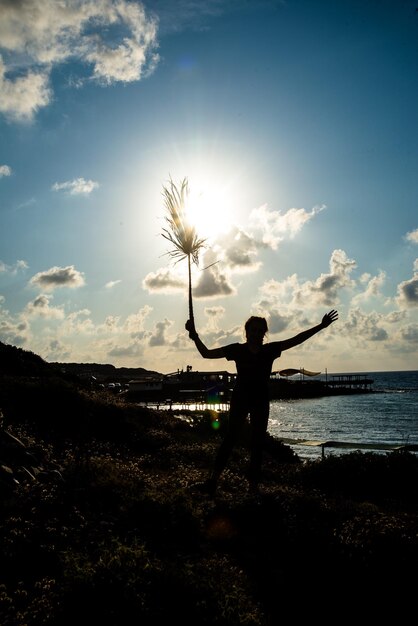 Photo silhouette d'une personne debout au bord de la mer contre le ciel au coucher du soleil