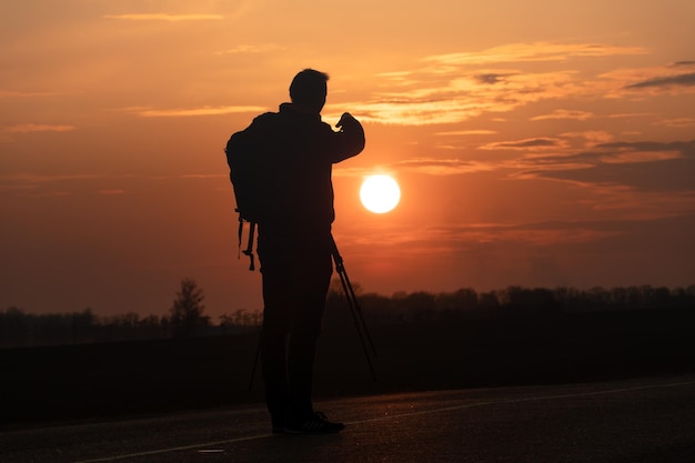 La silhouette d'une personne sur fond de soleil et de beau ciel Le contour d'un homme debout à côté d'un trépied et d'un appareil photo sur fond de coucher de soleil