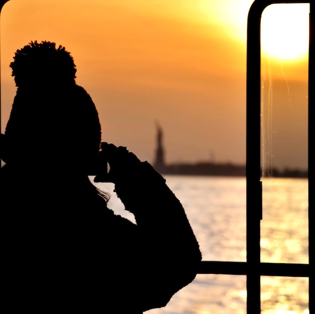 Photo silhouette d'une personne photographiant la mer au coucher du soleil