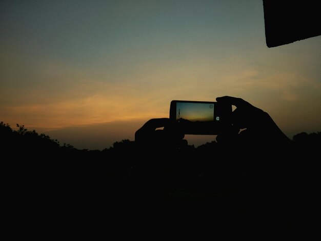 Photo silhouette d'une personne tenant un téléphone portable alors qu'elle photographie le ciel