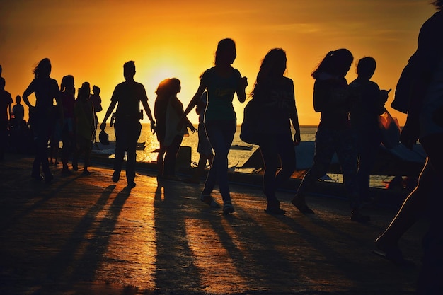 Silhouette de personnes marchant sur la mer contre le ciel au coucher du soleil