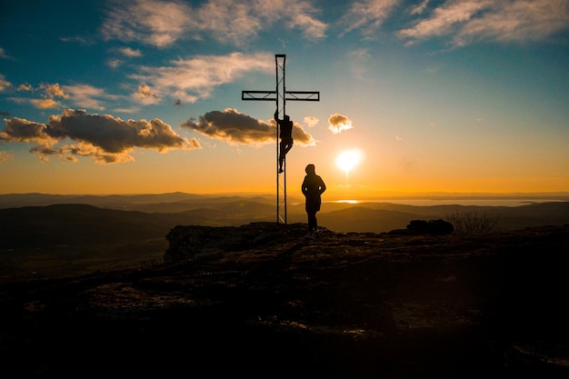 Silhouette de personnes par croix contre le ciel au coucher du soleil