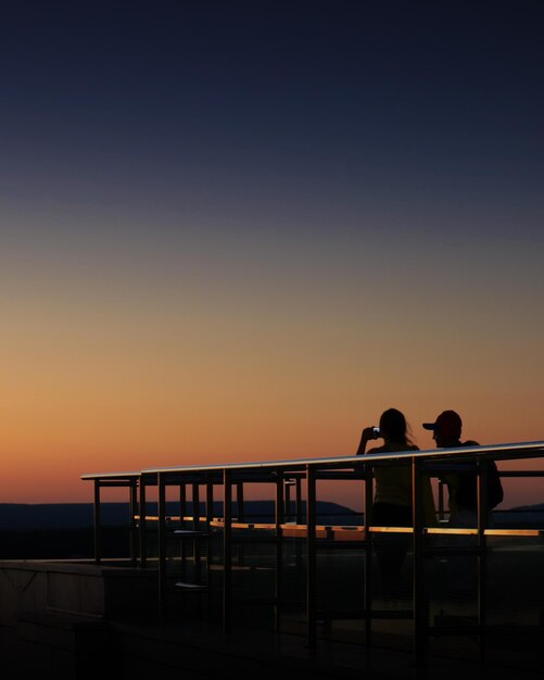 Photo silhouette de personnes sur une passerelle contre le ciel au coucher du soleil