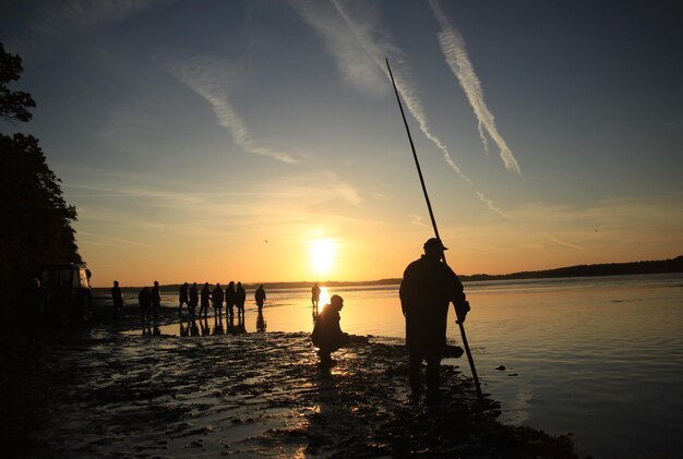 Photo silhouette de personnes sur la plage au coucher du soleil