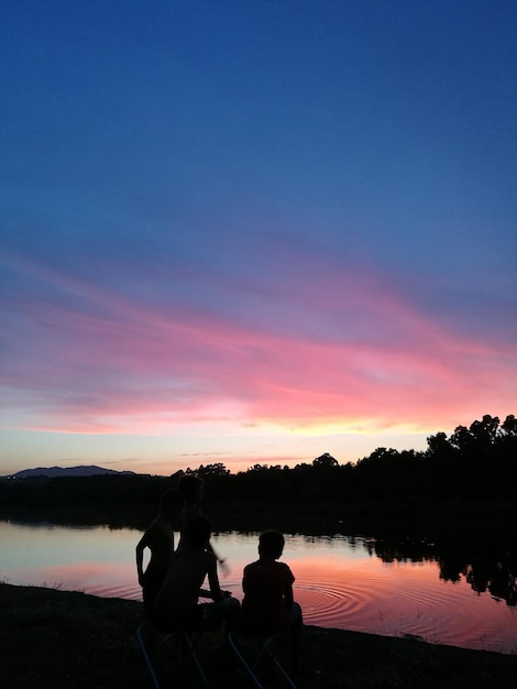 Photo silhouette de personnes près du lac contre le ciel au coucher du soleil