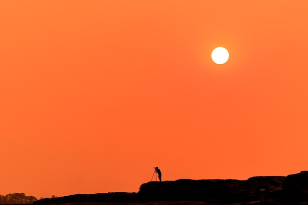 Silhouette petite du photographe prenant une photo sur la montagne et le fond du coucher de soleil