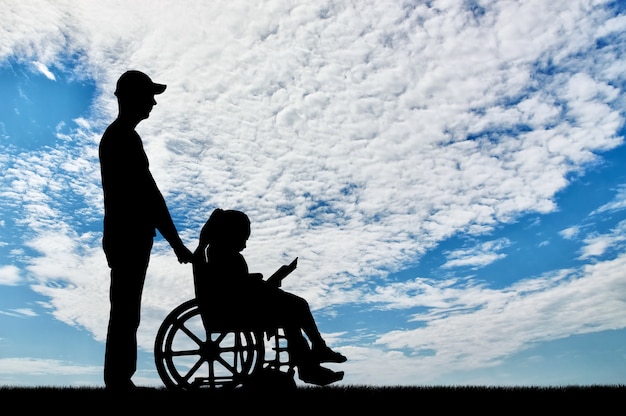 Silhouette d'une petite fille handicapée assise dans un fauteuil roulant, lisant un livre avec un père. Le concept de prise en charge des enfants handicapés