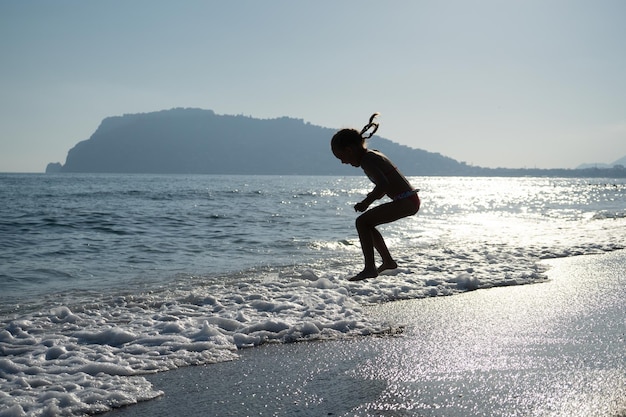 Silhouette d'une petite fille jouant sur la plage de la mer à la lumière des vacances au soleil couchant