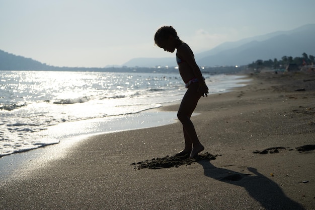 Silhouette d'une petite fille jouant sur la plage de la mer à la lumière des vacances au soleil couchant