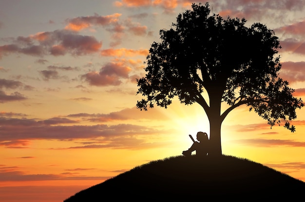 Silhouette d'une petite fille lisant un livre sous un arbre. La notion d'enfance