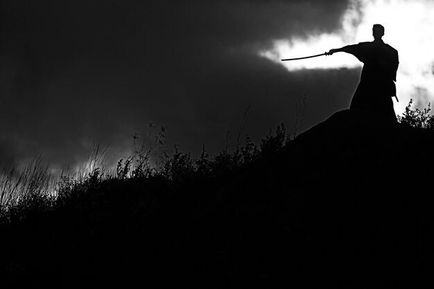 Silhouette photo noir et blanc du guerrier avec l'épée sur la montagne