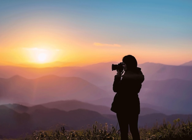 Silhouette d'un photographe qui filme un coucher de soleil sur les montagnes