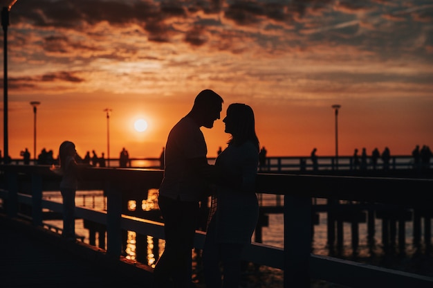 Silhouette de portrait d'un beau couple de jeunes mariés. Un homme aimant embrasse une fille au coucher du soleil, sur fond de mer debout sur la jetée.