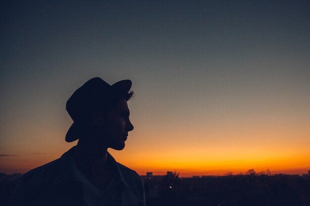 Silhouette d'un portrait d'homme, regardant le coucher de soleil sur la ville. Homme urbain avec chapeau. Beau.