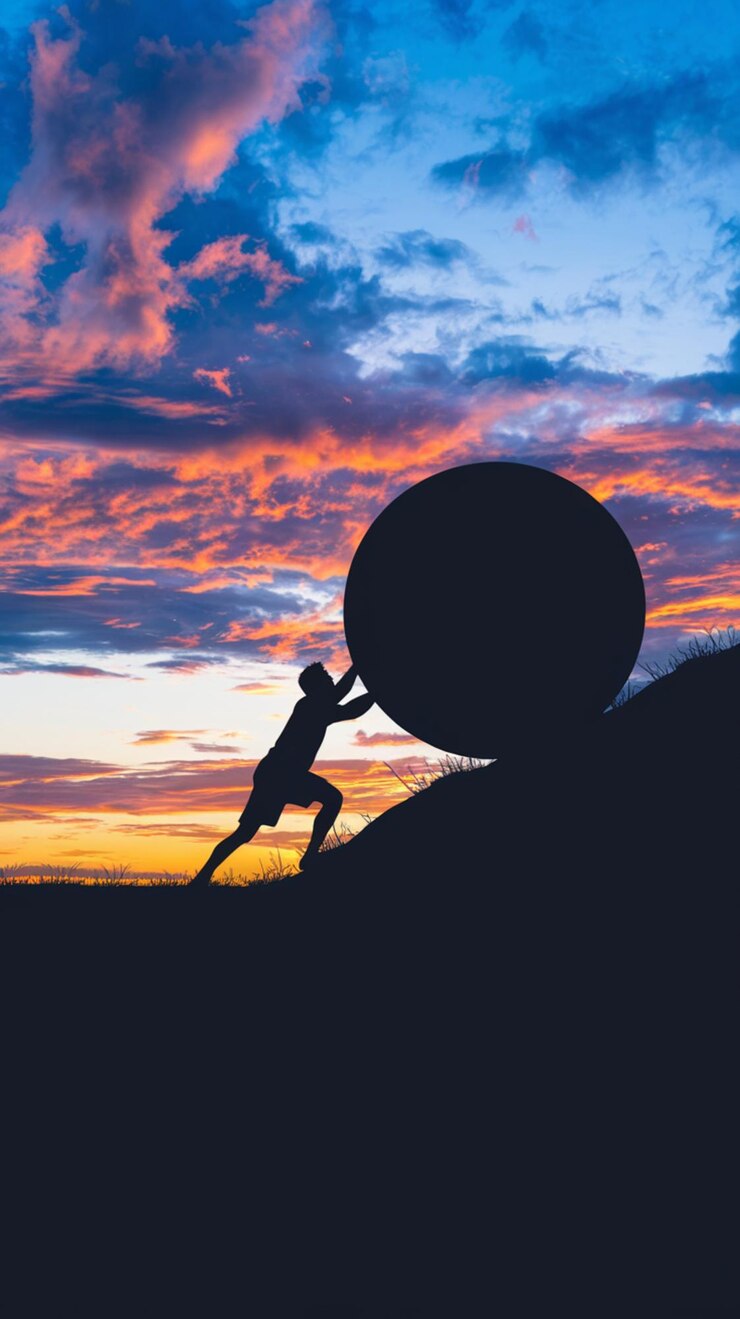 Photo silhouette poussant un rocher en amont coucher de soleil dramatique mettant en évidence la lutte