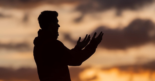 Silhouette de prière ayant le culte et priant avec les mains ouvertes au coucher du soleil