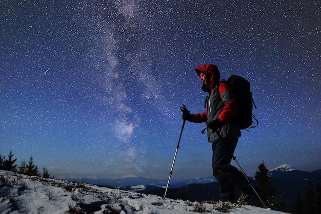 Silhouette solitaire d'un randonneur mâle adulte au sommet d'une montagne enneigée en prévision de l'aube Ciel étoilé sur fond