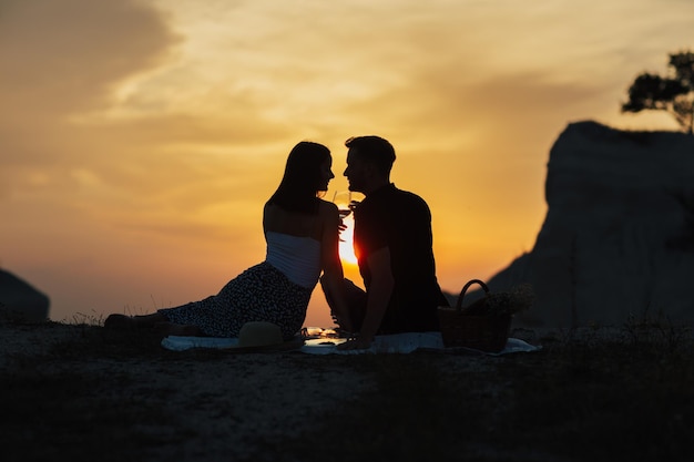 Silhouette sombre du couple au pique-nique sur fond de coucher de soleil orange