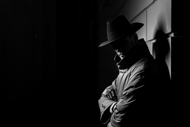 Silhouette sombre d'un homme dans un imperméable avec un chapeau la nuit dans la rue